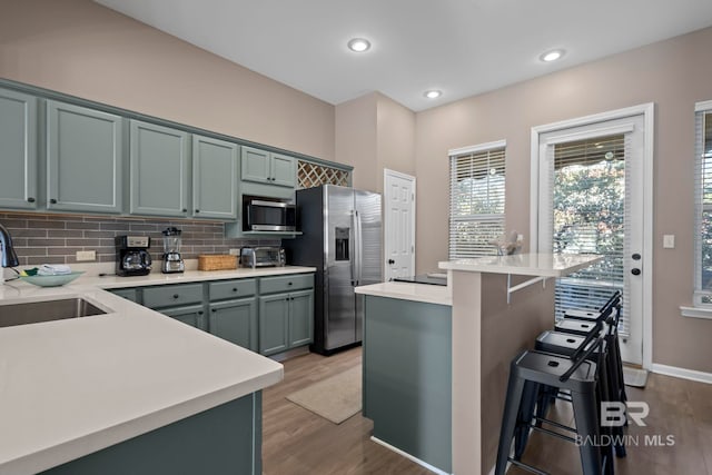 kitchen with backsplash, a kitchen breakfast bar, sink, light hardwood / wood-style flooring, and stainless steel appliances