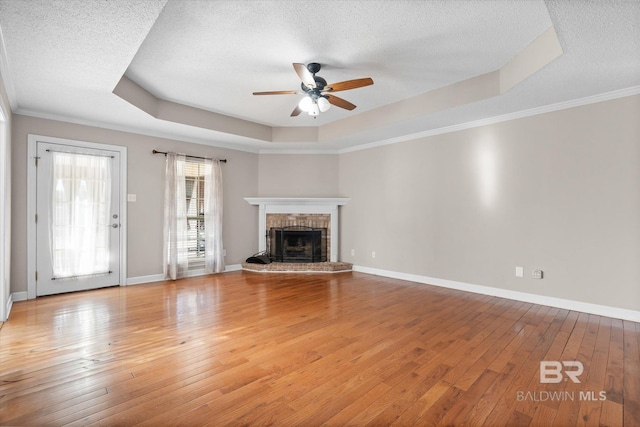 unfurnished living room featuring a brick fireplace, a raised ceiling, a textured ceiling, and light wood-type flooring