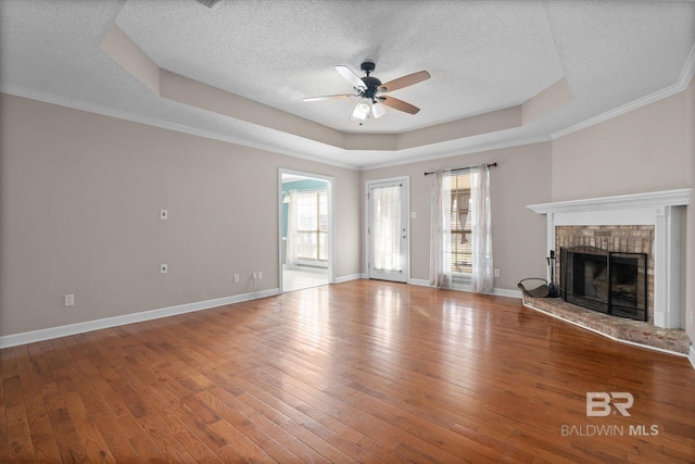 unfurnished living room featuring a brick fireplace, a textured ceiling, a raised ceiling, ceiling fan, and hardwood / wood-style floors