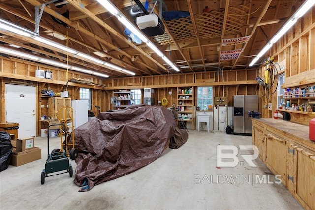 garage with sink, stainless steel fridge, a workshop area, and a garage door opener