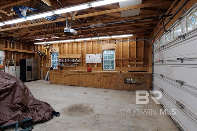 garage with a workshop area, a garage door opener, and stainless steel fridge with ice dispenser