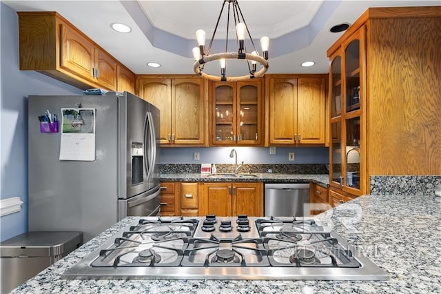 kitchen with sink, appliances with stainless steel finishes, a raised ceiling, and light stone counters