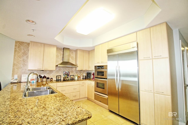 kitchen featuring sink, light brown cabinets, wall chimney range hood, kitchen peninsula, and appliances with stainless steel finishes