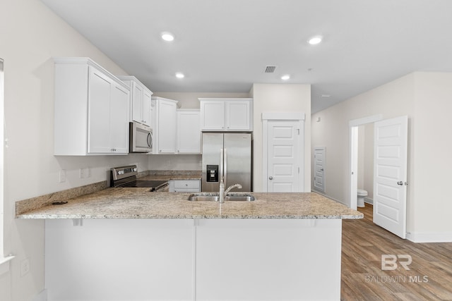 kitchen with sink, appliances with stainless steel finishes, kitchen peninsula, light stone countertops, and white cabinets