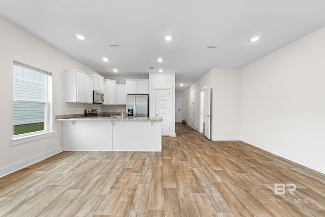 kitchen featuring stainless steel appliances, light stone countertops, white cabinets, kitchen peninsula, and light wood-type flooring