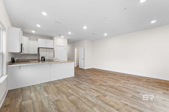 kitchen with white cabinetry, light stone counters, kitchen peninsula, stainless steel appliances, and light wood-type flooring