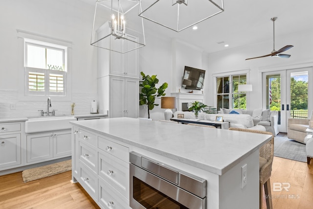 kitchen featuring hanging light fixtures, light wood-type flooring, ceiling fan, stainless steel microwave, and white cabinetry