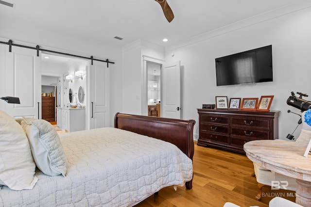 bedroom with ceiling fan, a barn door, connected bathroom, and light hardwood / wood-style floors