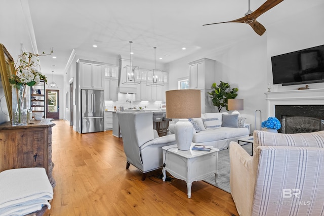 living room featuring ceiling fan with notable chandelier, light wood-type flooring, a high end fireplace, and a healthy amount of sunlight