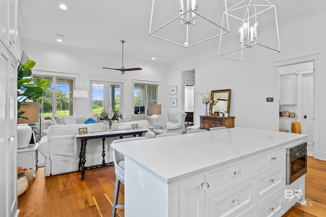 kitchen featuring ceiling fan with notable chandelier, hanging light fixtures, white cabinetry, light hardwood / wood-style flooring, and a center island