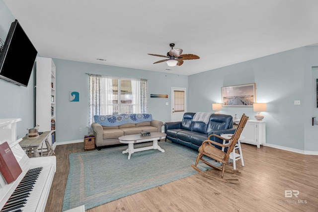 living area featuring baseboards, a ceiling fan, visible vents, and wood finished floors