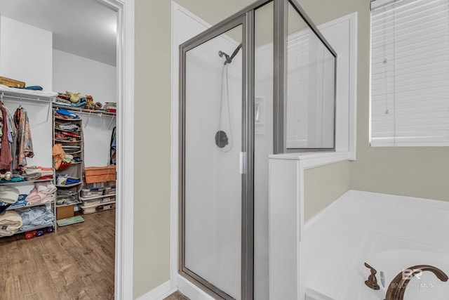 bathroom with a walk in closet, a garden tub, a shower stall, and wood finished floors