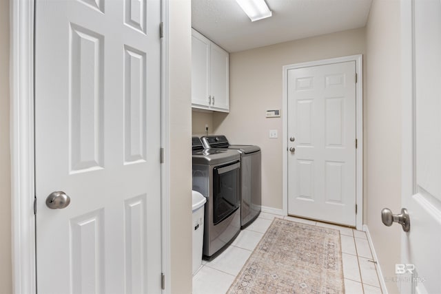 laundry room featuring cabinets, light tile patterned floors, a textured ceiling, and separate washer and dryer