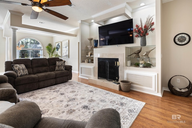 living room with decorative columns, ornamental molding, ceiling fan, hardwood / wood-style flooring, and a fireplace