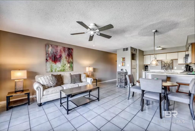 living area with light tile patterned floors, visible vents, a textured ceiling, and ceiling fan