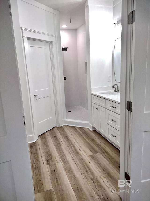 bathroom featuring vanity, a tile shower, and wood-type flooring