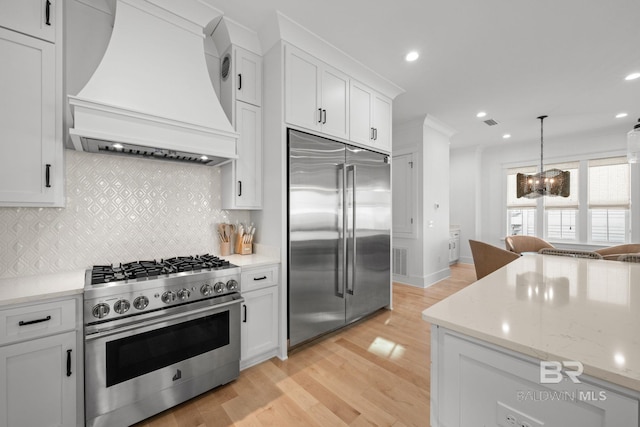 16761 Perdido Key Dr, Pensacola, FL 32507 - kitchen with light wood-type flooring, high end appliances, white cabinets, custom exhaust hood, and decorative backsplash