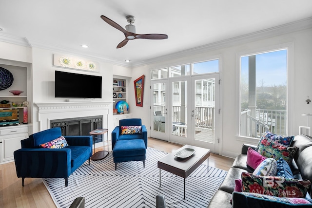 living room with crown molding, light wood-type flooring, ceiling fan, built in features, and a fireplace