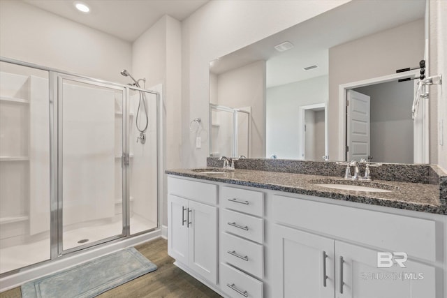 full bathroom featuring a shower stall, wood finished floors, double vanity, and recessed lighting