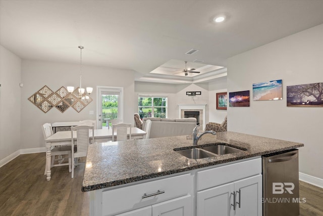 kitchen with a sink, dishwasher, a kitchen island with sink, baseboards, and a tray ceiling
