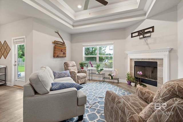 living room featuring ornamental molding, wood finished floors, ceiling fan, baseboards, and a tile fireplace