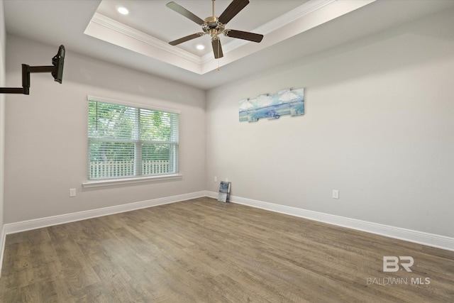 unfurnished room featuring ornamental molding, a raised ceiling, wood finished floors, ceiling fan, and baseboards