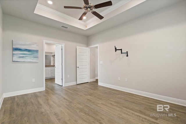 unfurnished bedroom with crown molding, a raised ceiling, wood finished floors, baseboards, and recessed lighting