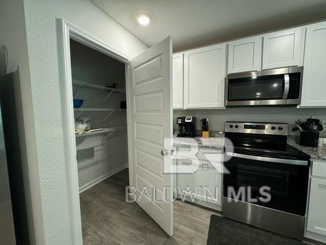 32807 N Pickens Ave, Lillian, AL 36549 - kitchen featuring stainless steel appliances, white cabinetry, light stone countertops, and light wood-style flooring