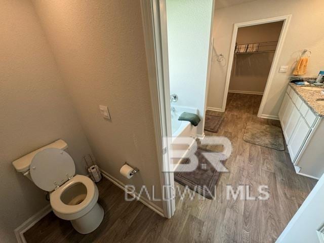 32807 N Pickens Ave, Lillian, AL 36549 - bathroom featuring wood finished floors, toilet, vanity, baseboards, and a spacious closet