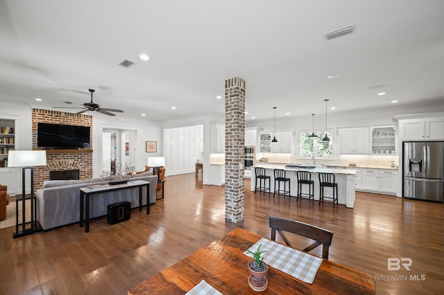 dining area with dark wood-type flooring, ornate columns, a fireplace, and ceiling fan