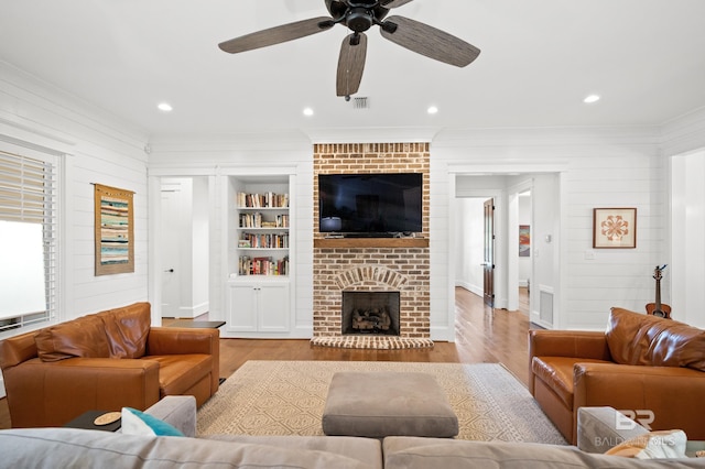 living room with light hardwood / wood-style flooring, a brick fireplace, built in shelves, and ceiling fan