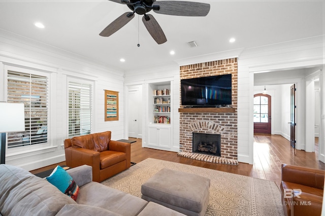 living room with ceiling fan, a brick fireplace, light wood-type flooring, and built in shelves