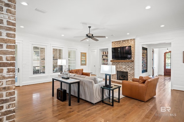 living room with brick wall, crown molding, a brick fireplace, light hardwood / wood-style floors, and ceiling fan