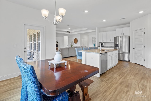 kitchen with a tray ceiling, appliances with stainless steel finishes, a sink, and light wood-style floors