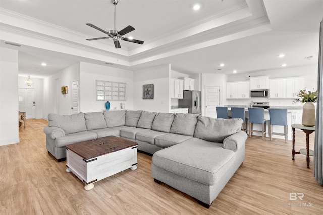 living room featuring ornamental molding, a tray ceiling, light wood-style flooring, and visible vents