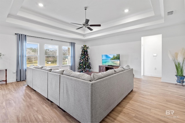 living area with a tray ceiling, light wood-type flooring, and crown molding