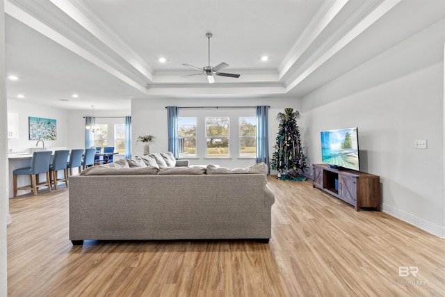 living room featuring baseboards, a raised ceiling, ornamental molding, light wood-type flooring, and recessed lighting