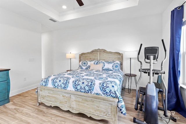 bedroom featuring a tray ceiling, wood finished floors, visible vents, and crown molding