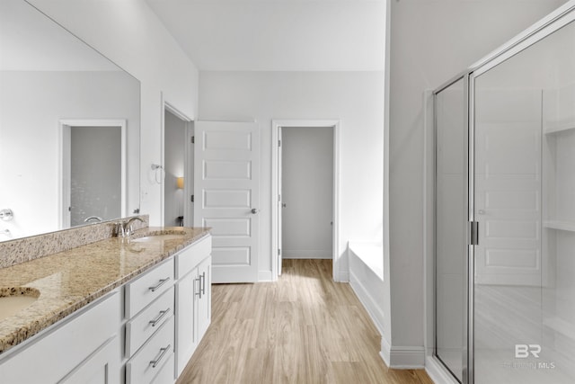 bathroom featuring double vanity, wood finished floors, a garden tub, a shower stall, and a sink