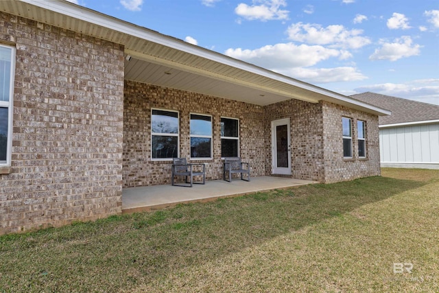 back of property with brick siding, a lawn, and a patio