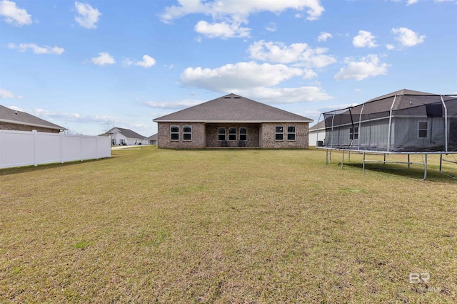 rear view of property featuring a trampoline, brick siding, a yard, and fence