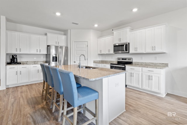 kitchen with a center island with sink, light wood-style flooring, stainless steel appliances, a kitchen bar, and a sink