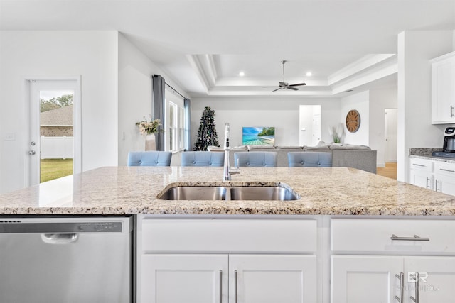 kitchen with light stone counters, a raised ceiling, white cabinets, a sink, and dishwasher