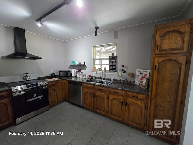 kitchen with wall chimney range hood, track lighting, stainless steel appliances, and sink