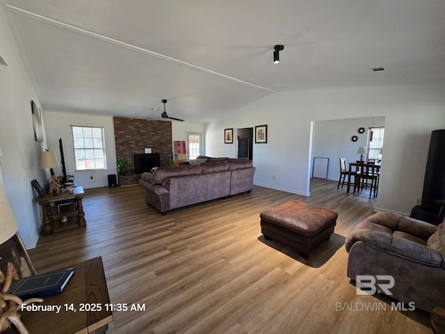 living room featuring hardwood / wood-style flooring, vaulted ceiling, a brick fireplace, and ceiling fan