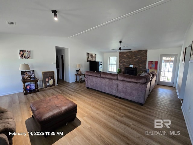 living room featuring lofted ceiling, hardwood / wood-style floors, a healthy amount of sunlight, and a brick fireplace