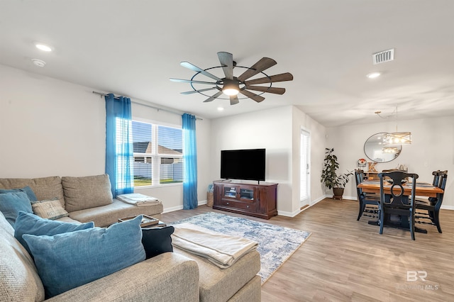 living room featuring a ceiling fan, baseboards, recessed lighting, light wood-type flooring, and a chandelier