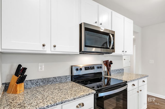 kitchen featuring stainless steel microwave, electric range, white cabinets, light stone countertops, and wood finished floors