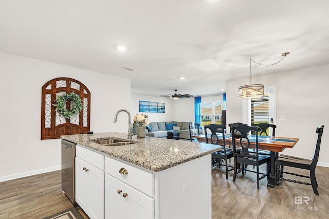 kitchen with a sink, stainless steel dishwasher, light wood-style floors, baseboards, and light stone counters