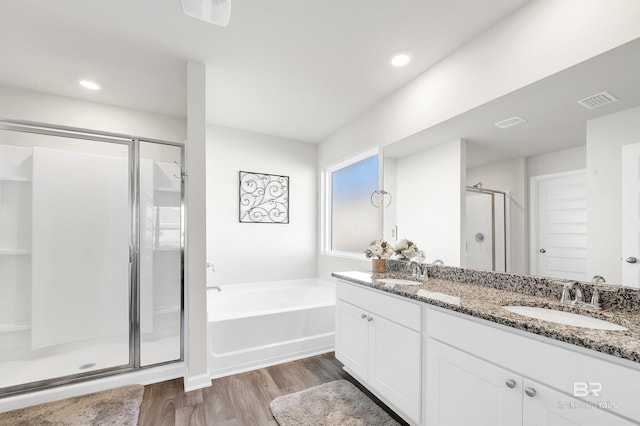bathroom with a shower stall, wood finished floors, a bath, double vanity, and recessed lighting